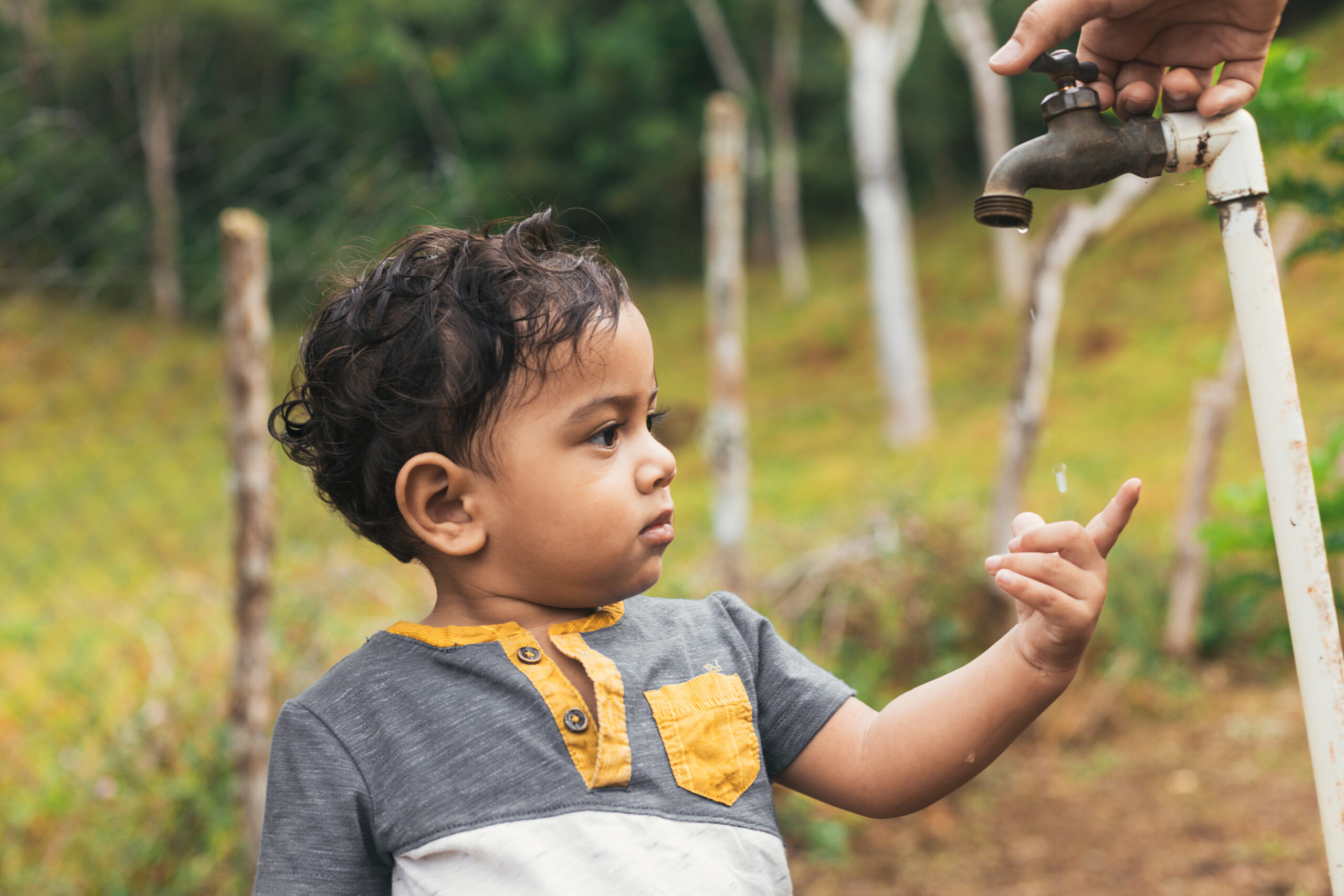 Latin boy touching the drops of water that come out of the faucet,